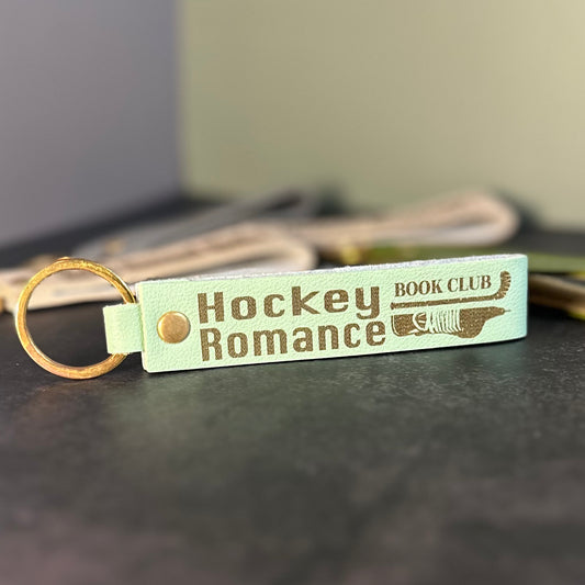 A matcha green faux-leather keychain with 'Hockey romance book club' etched into it.