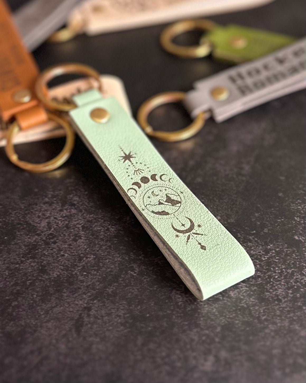 A matcha green faux-leather keychain with moons and mountains etched into it.